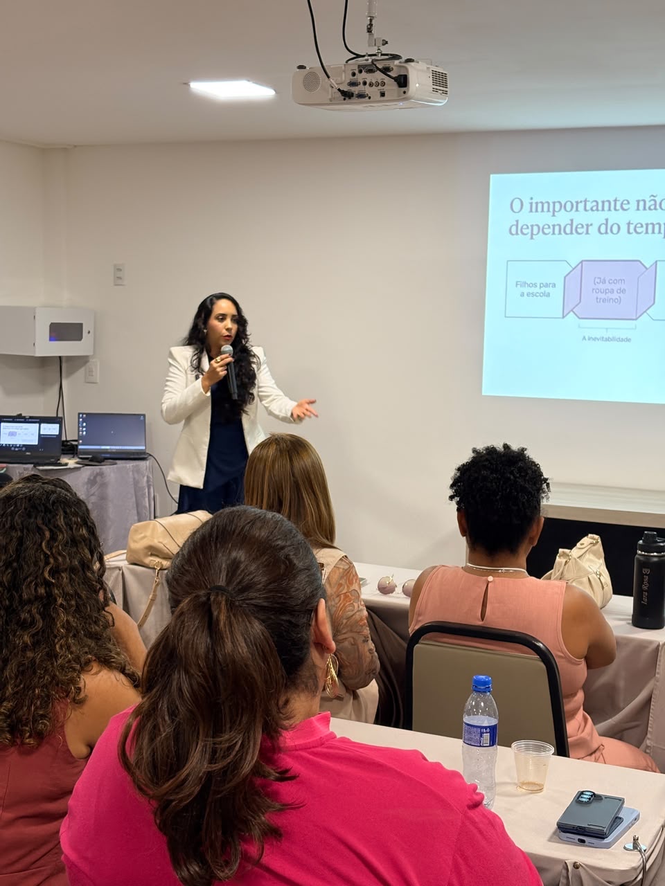 Aghata Zequetto apresenta a palestra com microfone e gesto aberto