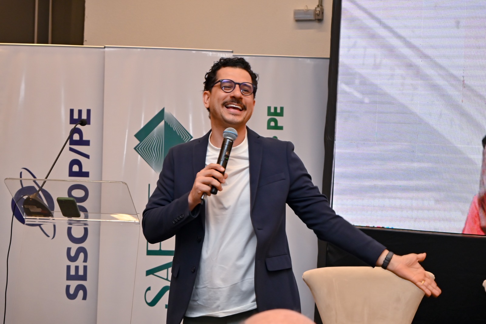 Cleber Zequetto sorrindo e falando ao público durante o Coopanest Day PE